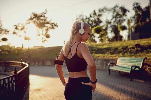 Κορίτσι σε ακουστικά για ένα τρέξιμο στο πάρκο στο ηλιοβασίλεμα. — Φωτογραφία Αρχείου