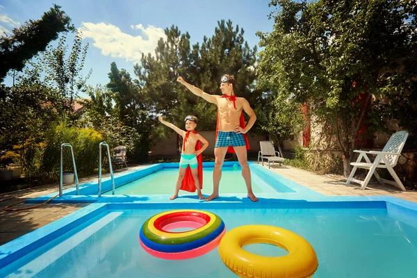 Father and son in suits of superheroes in the pool.