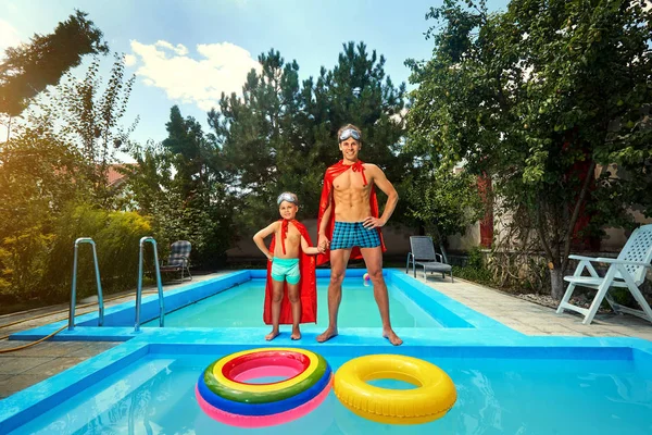 Padre e hijo en trajes de superhéroes en la piscina en el verano — Foto de Stock