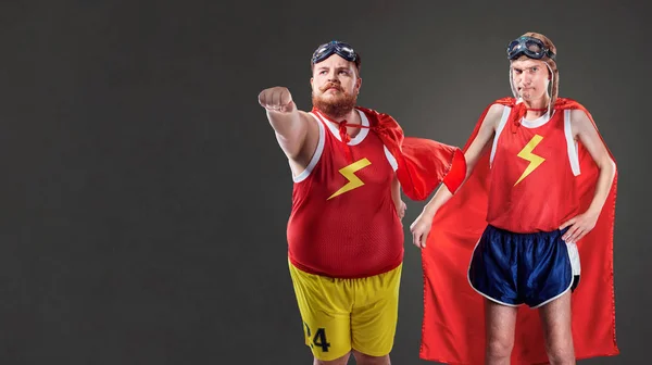Dos hombres divertidos con trajes de superhéroes. Personas delgadas y gordas —  Fotos de Stock