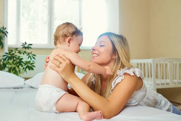 Mère et bébé dans une couche jouer câlins sur un lit à l'intérieur . — Photo