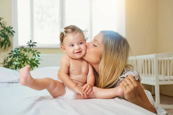 母亲和婴儿在一个尿布游戏中拥抱在室内的床上. — 图库照片