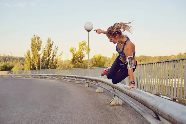 A girl runner jumps over a railing on a bridge in the city.