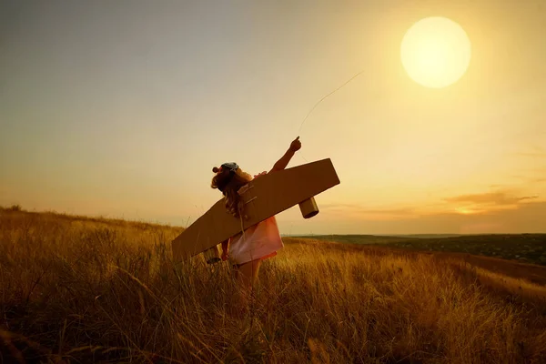 Malá holčička v šatech piloti v poli v přírodě při západu slunce. — Stock fotografie
