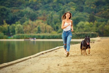 Bir kız, yaz park sahilinde köpeğiyle oynuyor.