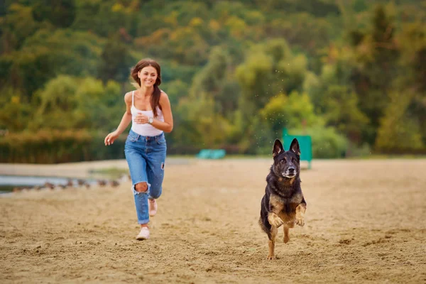 Bir kız, yaz park sahilinde köpeğiyle oynuyor.