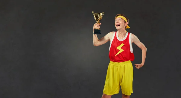 Divertido chico delgado en ropa deportiva con una copa de campeonato en su —  Fotos de Stock
