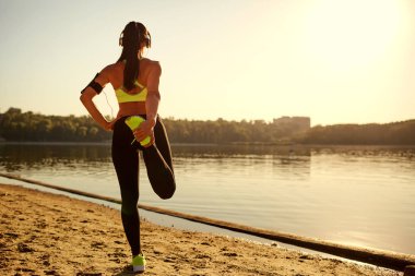 Genç kadın atlet bir parkta bacaklarını germe ısınma yapıyor.