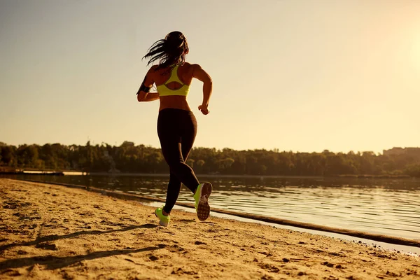 Uma jovem corredora corre ao pôr do sol em um parque no lago . — Fotografia de Stock