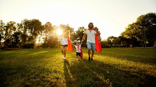 Gelukkige familie in pakken van superhelden in het park bij zonsondergang — Stockfoto