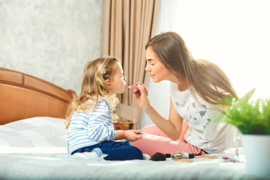 Anne ve kızı makyaj yapmak, pencerenin yanındaki yatakta oyun.