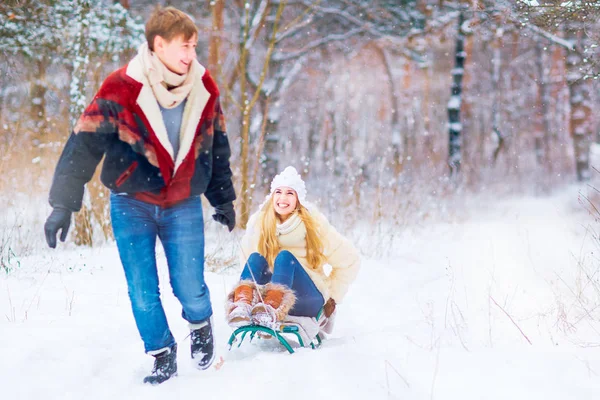 Um casal feliz está montando um trenó na neve em um parque na vitória — Fotografia de Stock