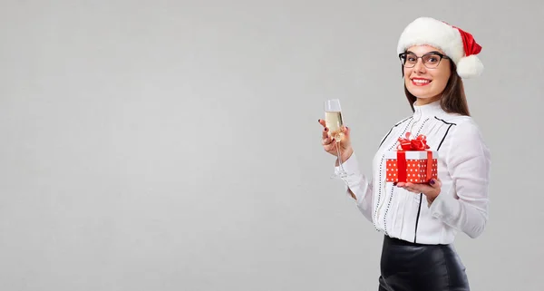 Uma menina em um chapéu de Papai Noel com uma taça de champanhe e um presente nele — Fotografia de Stock