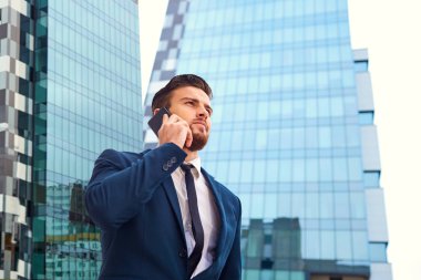 Sakallı bir bina karşı telefonda konuşurken bir işadamı