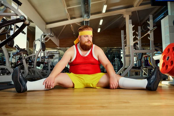 Gordo hombre divertido cansado sentado en el suelo en el gimnasio — Foto de Stock