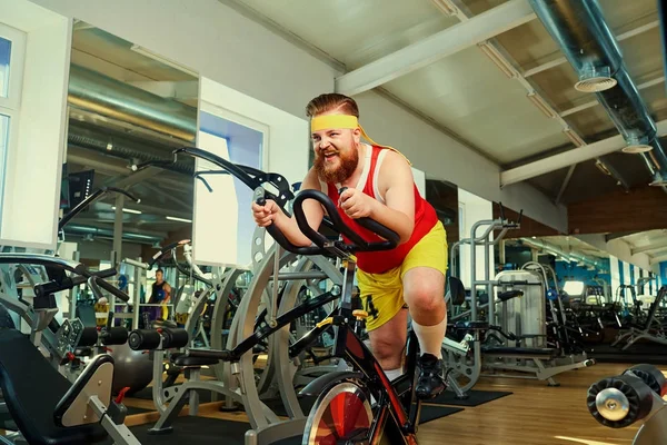A fat man is training on an exercise bike in the gym