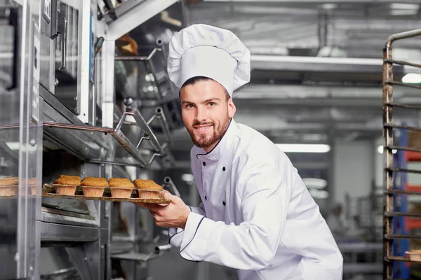 Um padeiro homem com uma bandeja de cupcakes . — Fotografia de Stock