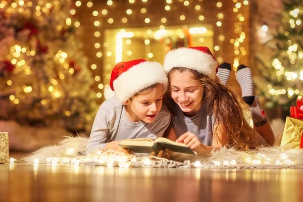 Duas crianças no chão leram um livro em um quarto com Natal — Fotografia de Stock