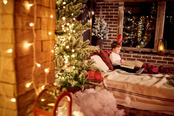 Een kleine jongen is het lezen van een boek in de kerst-kamer. — Stockfoto