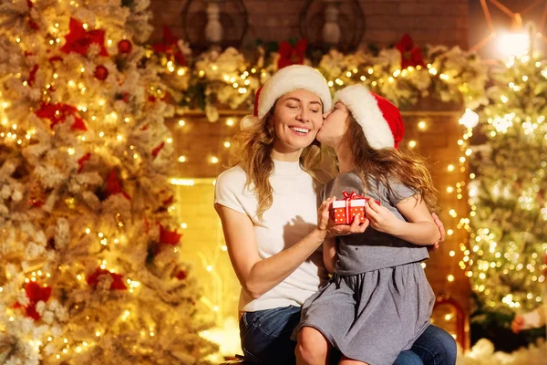Mother and daughter in Santa hats give presents in a room on Chr — Stock Photo, Image