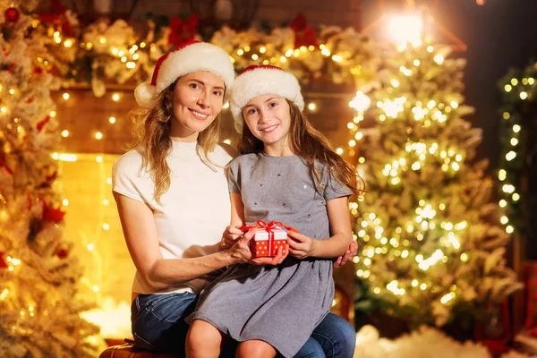 Moeder en dochter in Santa hoeden geven geschenken in een kamer op Chr — Stockfoto