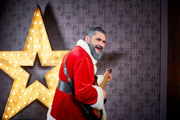 Fröhlicher Weihnachtsmann mit Gitarre tanzt vor dem Hintergrund eines — Stockfoto