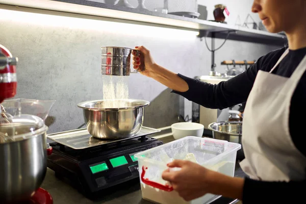 Una mujer tamiza la harina a través de un tamiz en la cocina — Foto de Stock