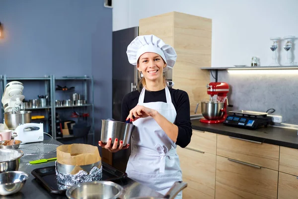 Una mujer pastelera con un pastel en la mano en la pastelería . — Foto de Stock