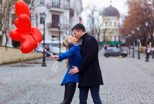 Una joven pareja en un abrigo sostiene un corazón de globos en la cit — Foto de Stock