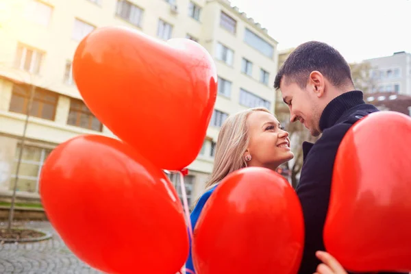 Una joven pareja en un abrigo sostiene un corazón de globos en la cit — Foto de Stock