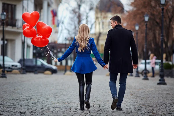 Una giovane coppia in cappotto sta tenendo un cuore palloncini nella cit — Foto Stock