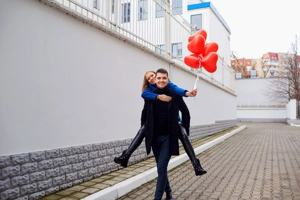 Meisje piggyback op kerel met rood hart ballonnen op straat. — Stockfoto
