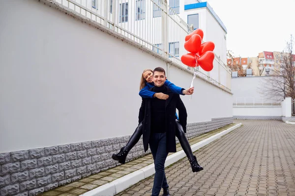 Dívka složená na chlápka s balónky červené srdce na ulici. — Stock fotografie