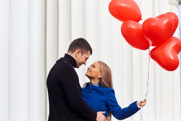 Una pareja cariñosa en un abrigo con globos rojos corazones en las manos . — Foto de Stock