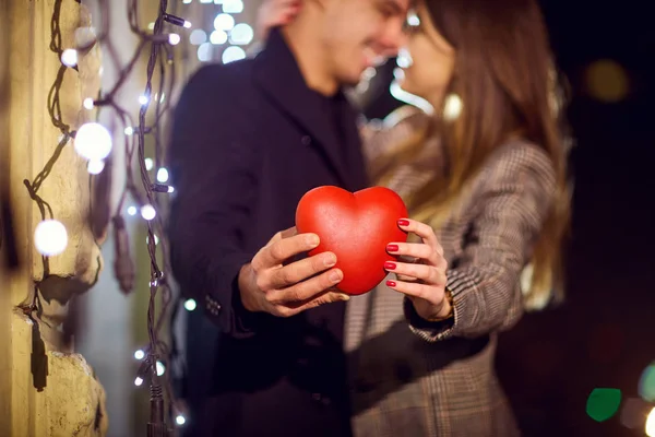 Rotes Herz in den Händen eines Paares bei Nacht im Bokeh-Licht. — Stockfoto