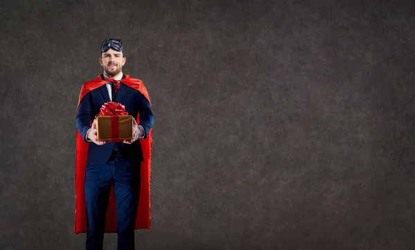 Un hombre con un disfraz de superhéroe con una caja de regalo en su lugar para el texto . — Foto de Stock