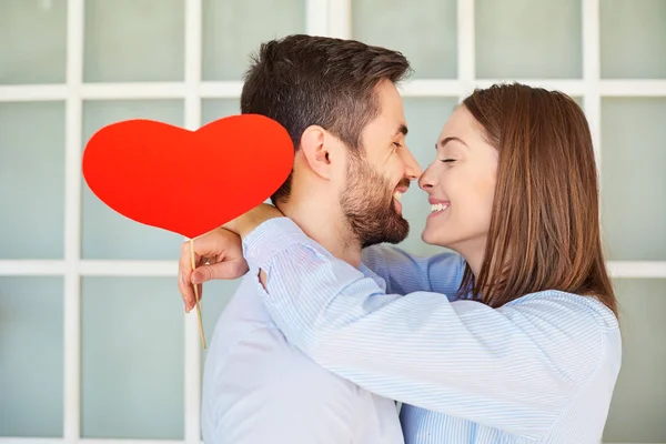 A loving couple with a red heart laugh. — Stock Photo, Image
