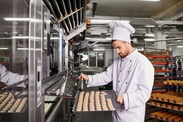 Um padeiro homem com uma bandeja de cupcakes em uma padaria — Fotografia de Stock