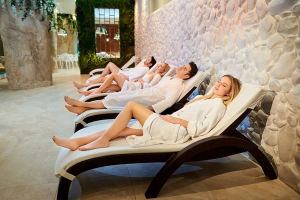 Las personas con albornoces están descansando en el salón de spa . — Foto de Stock