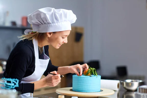 Uma mulher de confeiteiro decoração um bolo na cozinha . — Fotografia de Stock