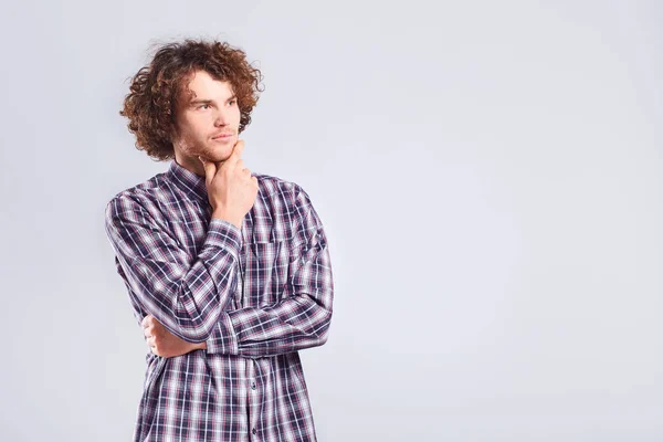 Een curly-haired man denkt met een ernstige emotie. — Stockfoto