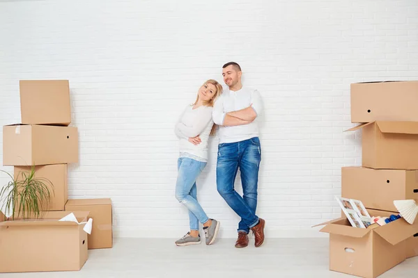 Una coppia con scatole si trasferisce in una nuova casa contro un muro bianco . — Foto Stock