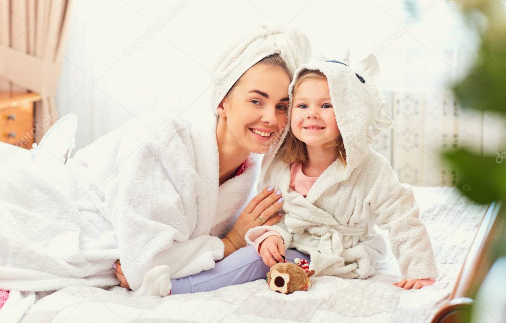 Mother and daughter in bathrobes and towels on the bed in the ro