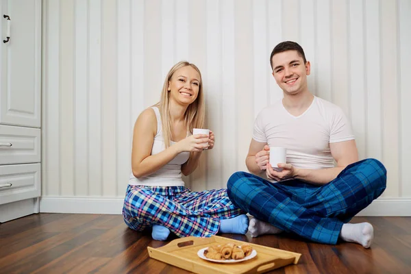Um casal feliz de pijama sentar no chão uma parede listrada backgr — Fotografia de Stock