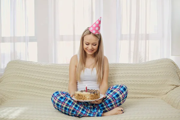 Una chica rubia en una gorra de pijama con un pastel con una vela celebrat — Foto de Stock
