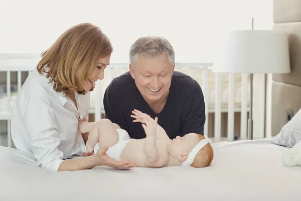 Abuelos y el bebé están jugando en la cama . — Foto de Stock