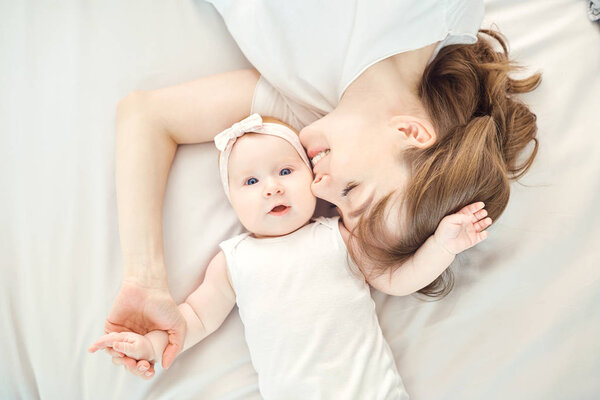 Top view of a happy mother kissing a baby lying on a bed.