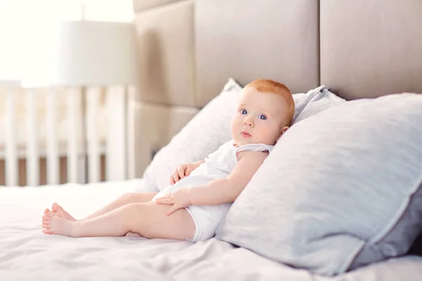 Funny baby is sitting on a pillow on the bed. — Stock Photo, Image