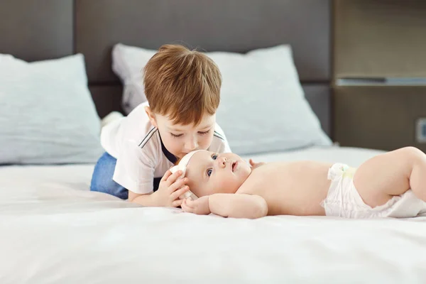 En liten pojke med sin lillasyster puss och kram på sängen. — Stockfoto