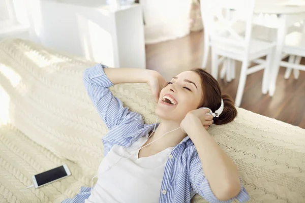 Chica en auriculares sonriendo escuchando música sentada . — Foto de Stock